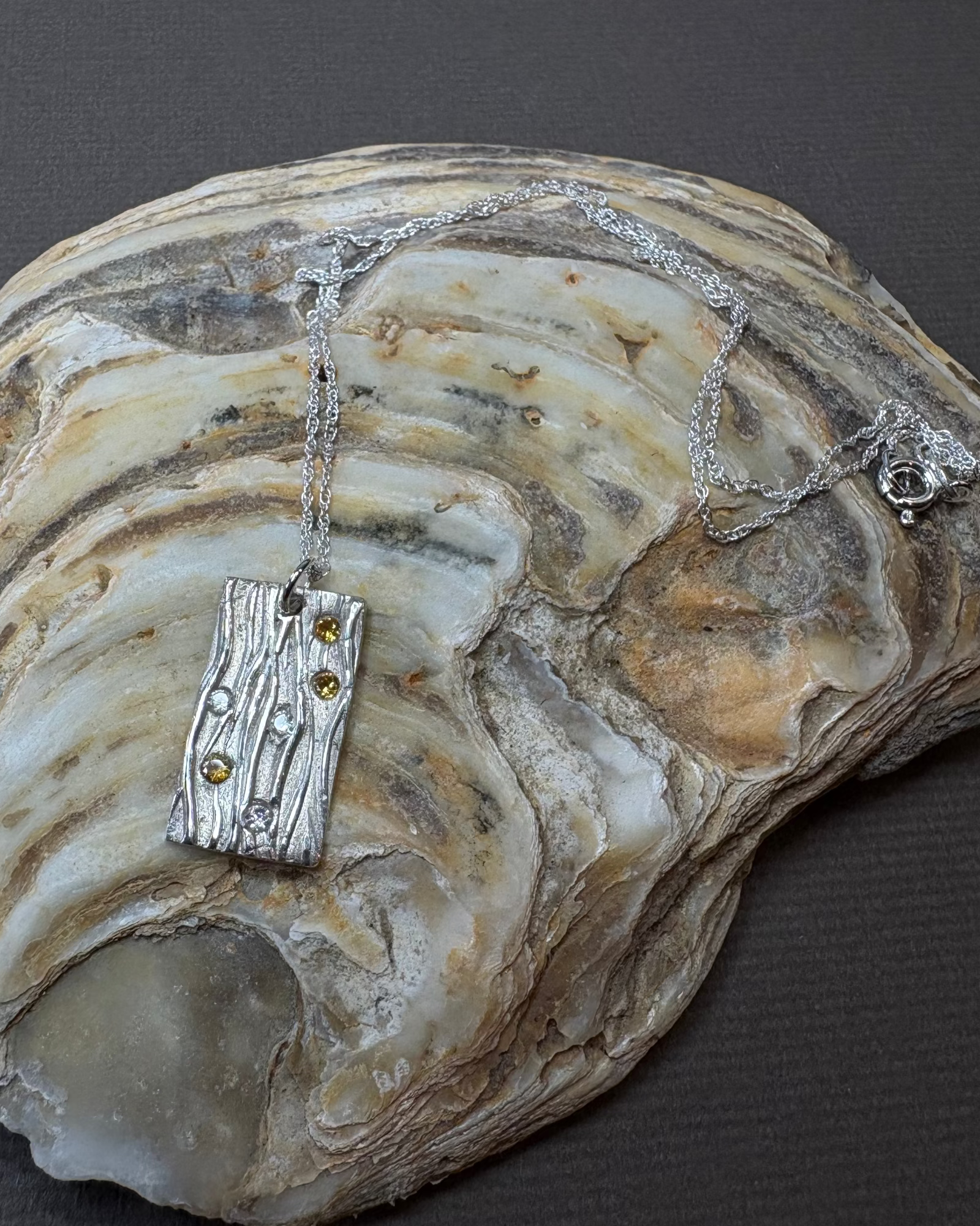 Silver stream necklace with gold and clear cubic zirconia with a silver chain, on an oyster shell
