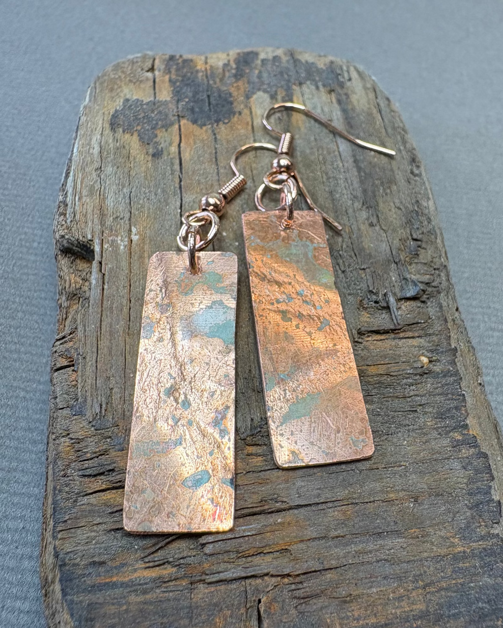 Pair of copper oxidised and textured earrings on a piece of driftwood