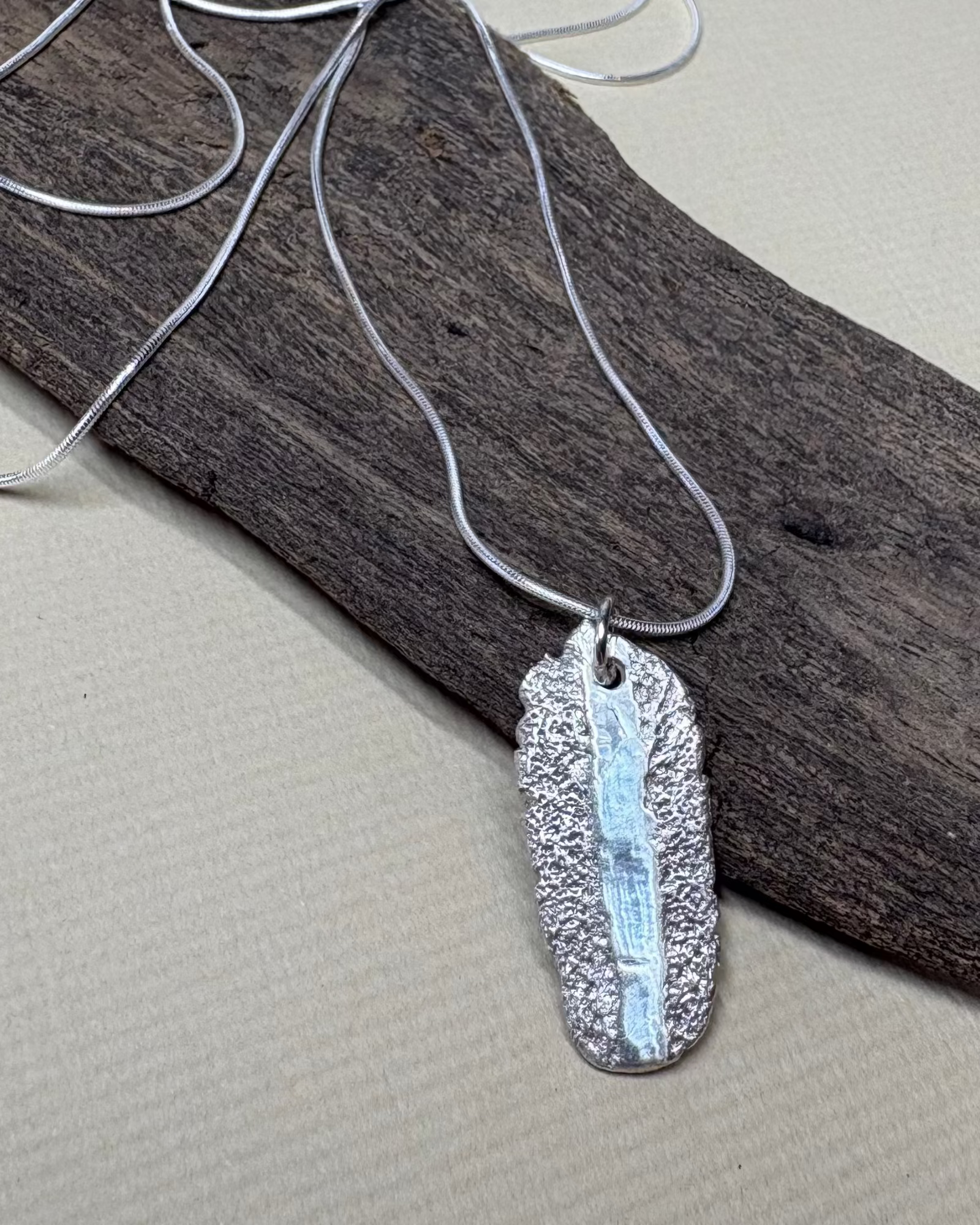 Silver rough and smooth texture oval necklace with silver chain on driftwood