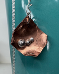 Copper pendant necklace with  curled corners and 3 silver satellite orbs with a silver chain on a teal mug