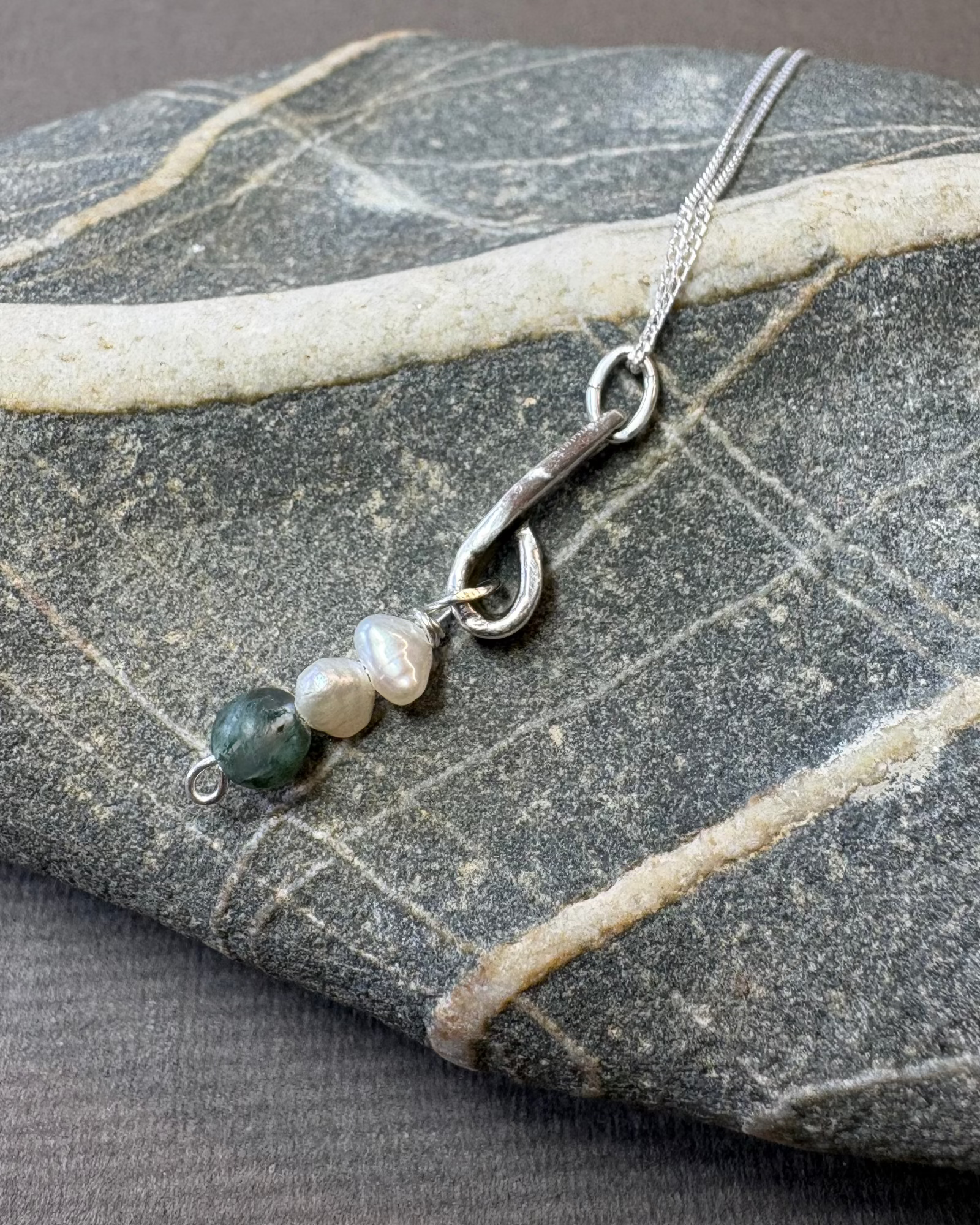 Silver necklace with pearls and moss agate beads on a pebble surface