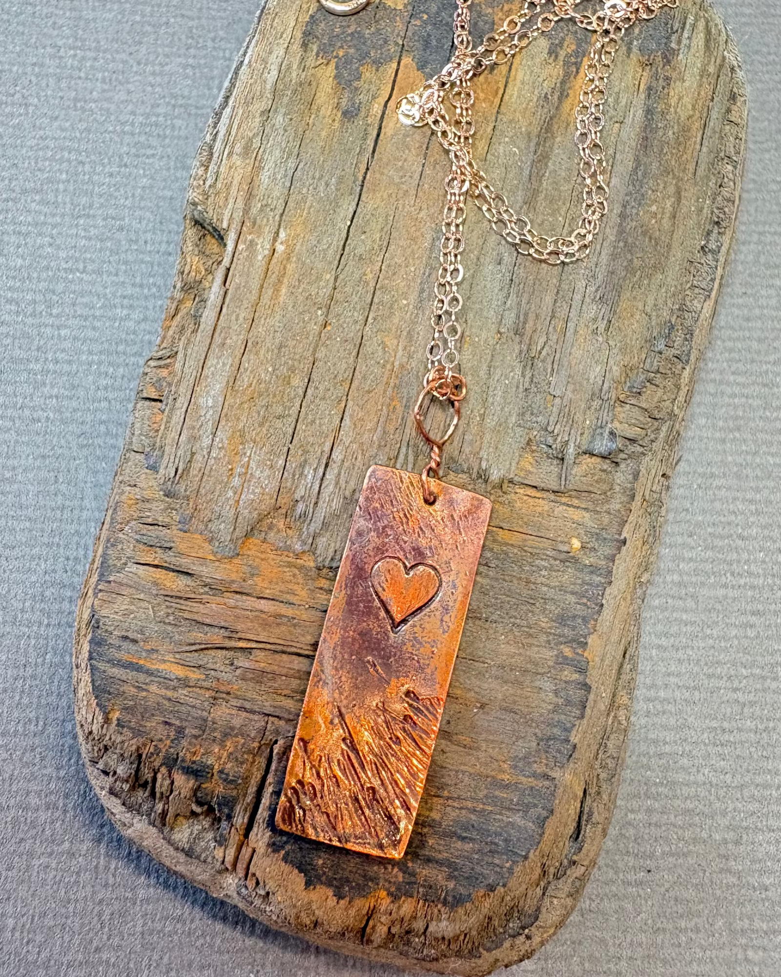 Copper necklace with a heart stamp on a driftwood block 