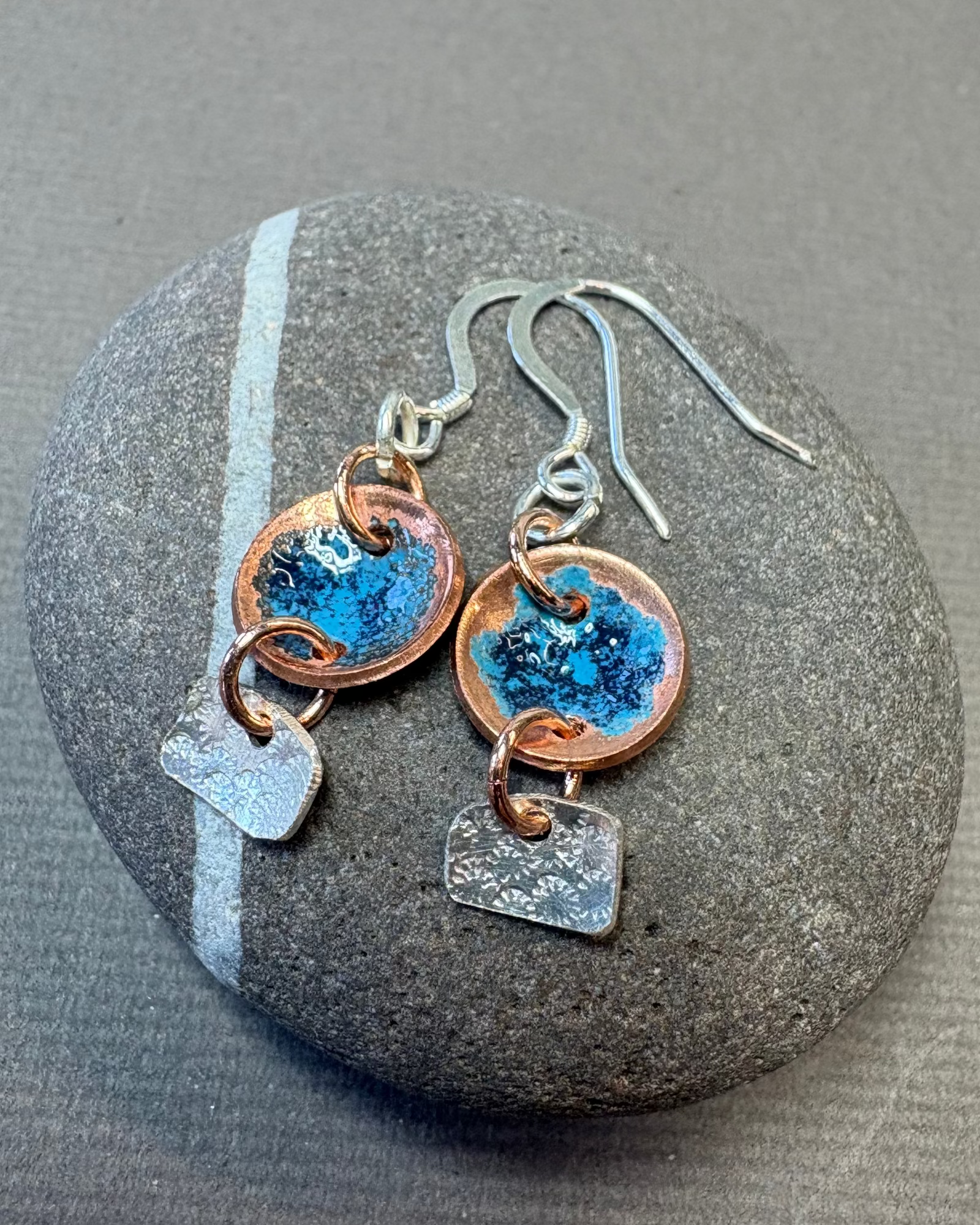 Pair of copper and silver earrings with blue enamel design on a pebble