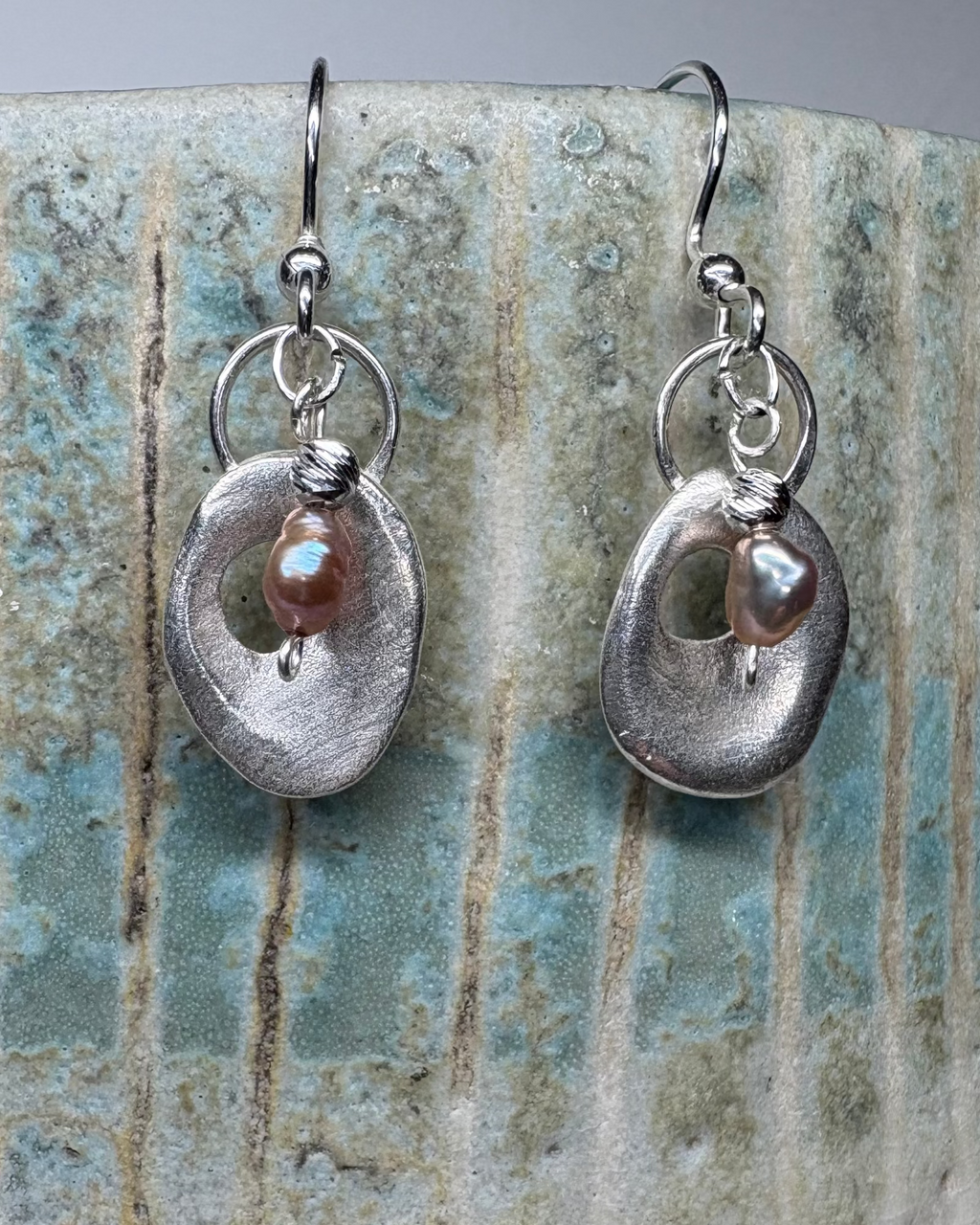 Silver earrings with pink pearls on a textured ceramic surface