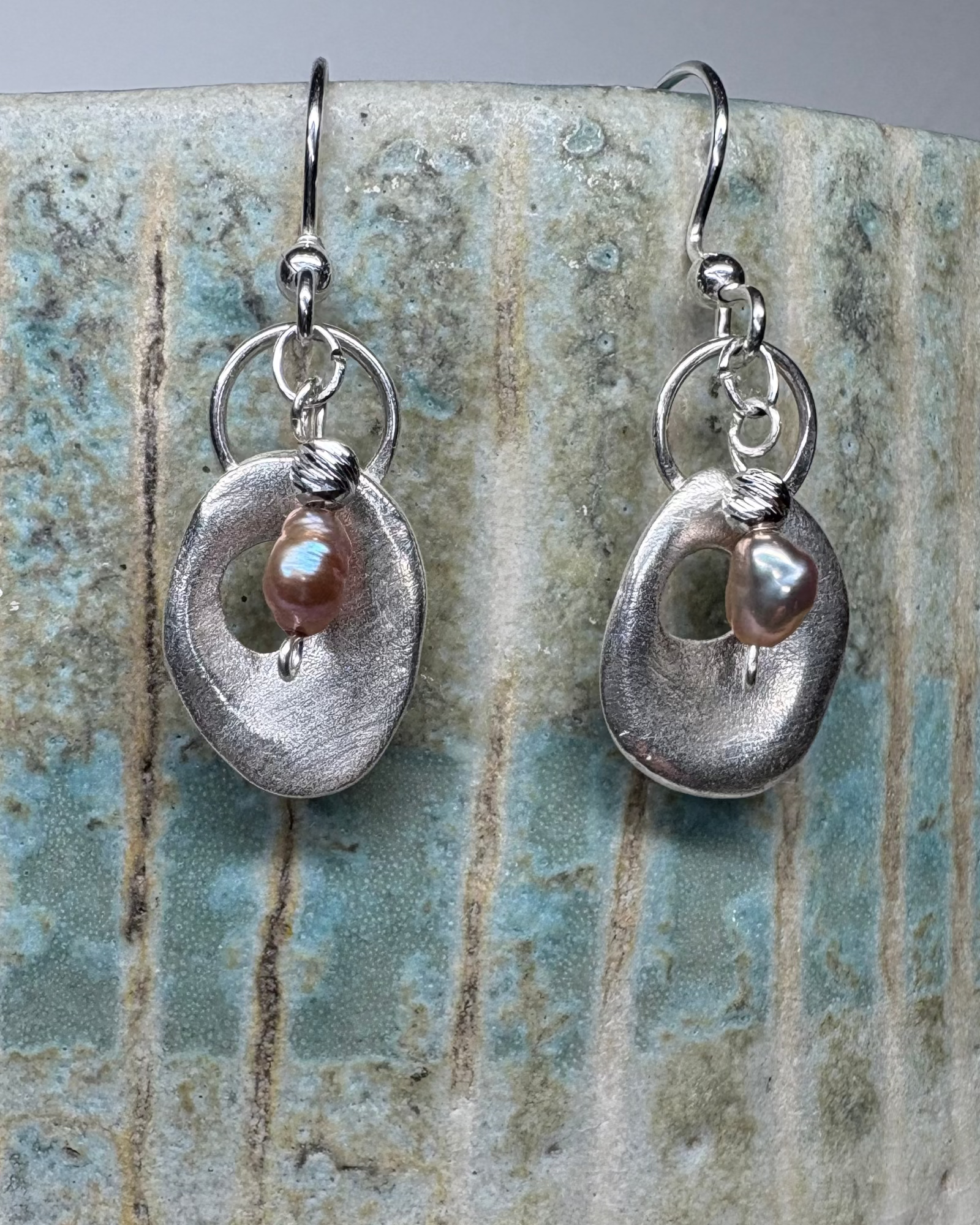 Silver earrings with pink pearls on a textured ceramic surface