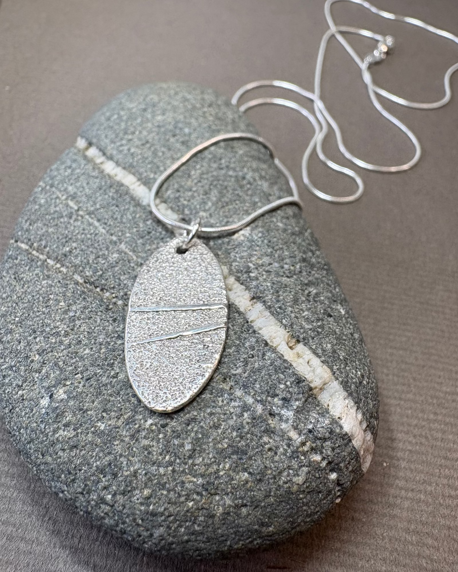 Silver textured pebble pendant necklace on a textured pebble surface
