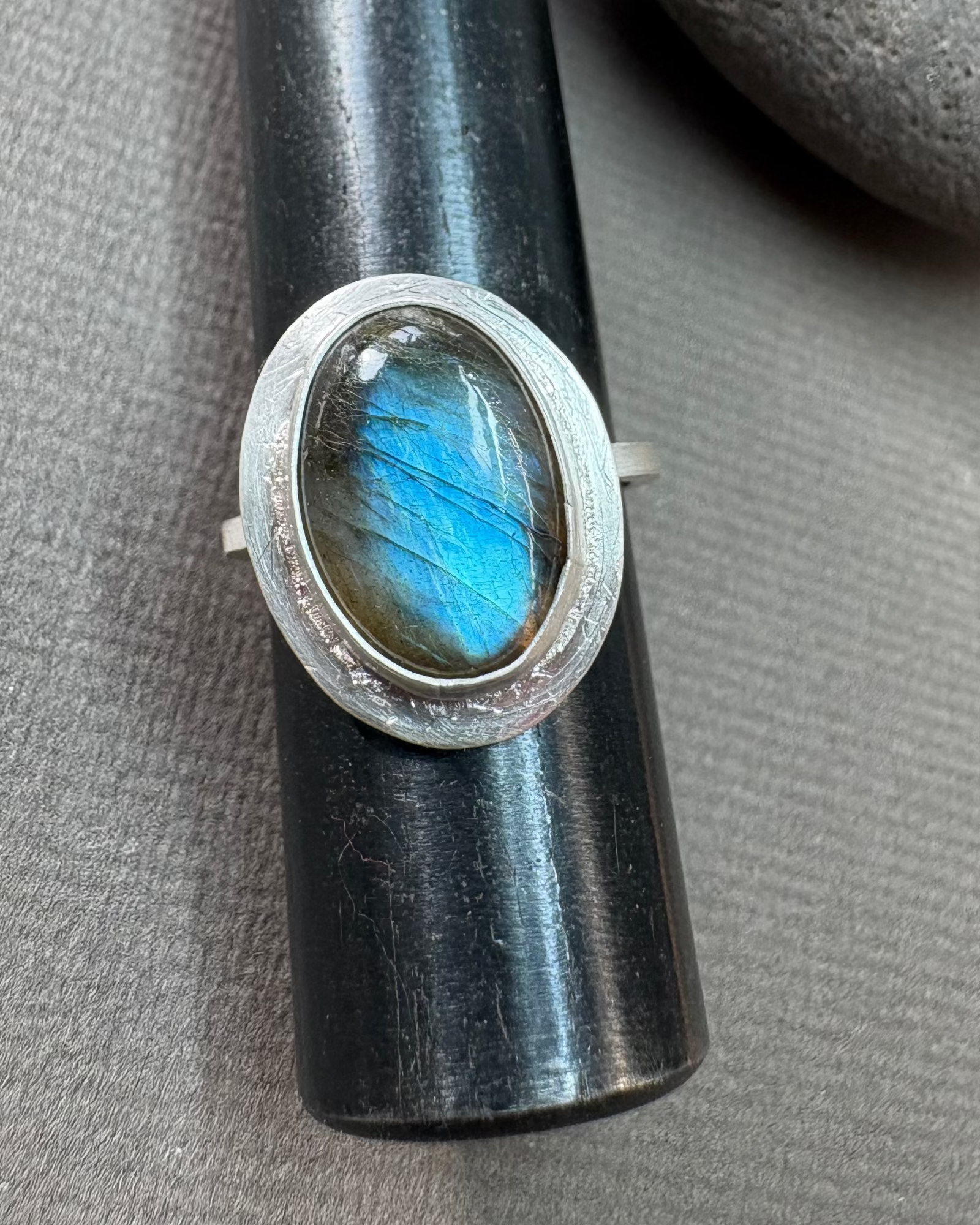 Silver ring with a bezel set labradorite gemstone on a grey surface