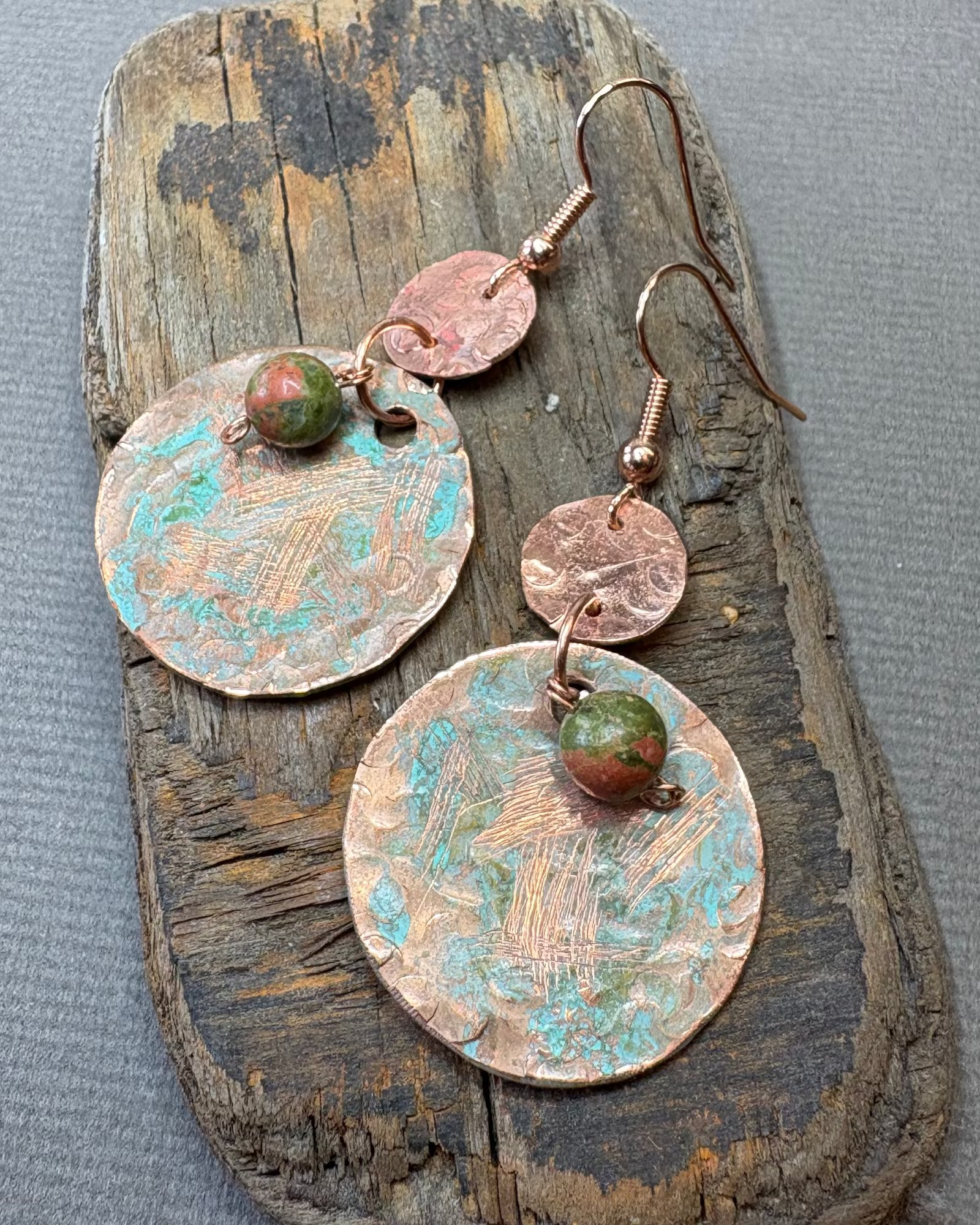 Pair of copper and turquoise oxidised earrings with unakite beads on a piece of driftwood