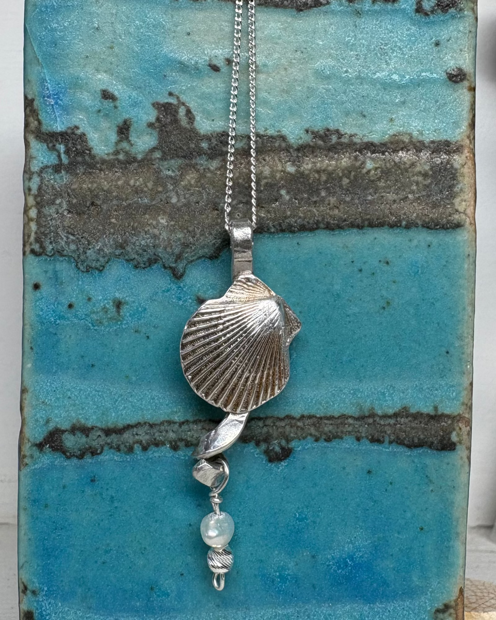 Silver necklace with a shell and pearl pendant on a textured blue surface