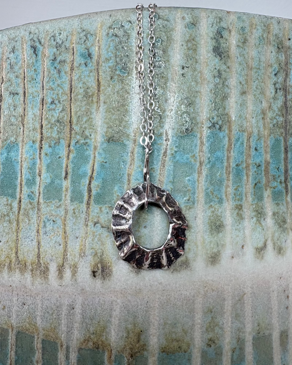 Silver sea-worn limpet shell pendant on a textured ceramic surface