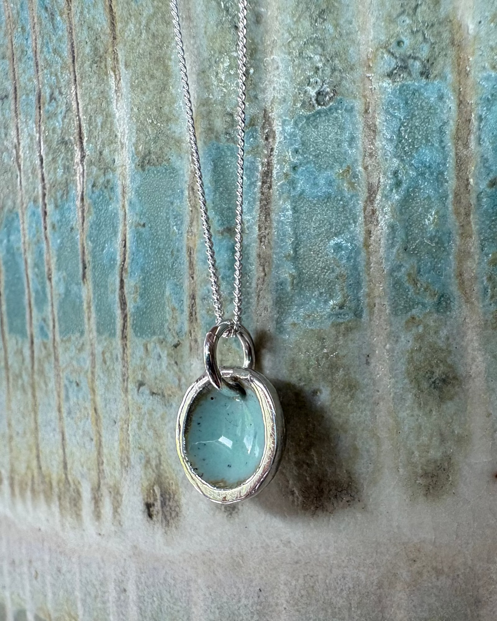Silver pool necklace with a turquoise enamel centre on a textured surface