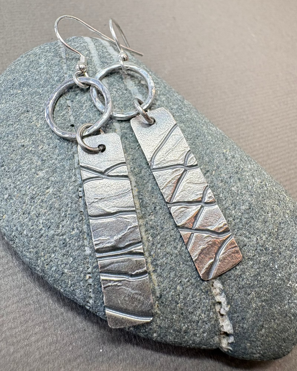 Silver hoop earrings with textured design on a pebble surface