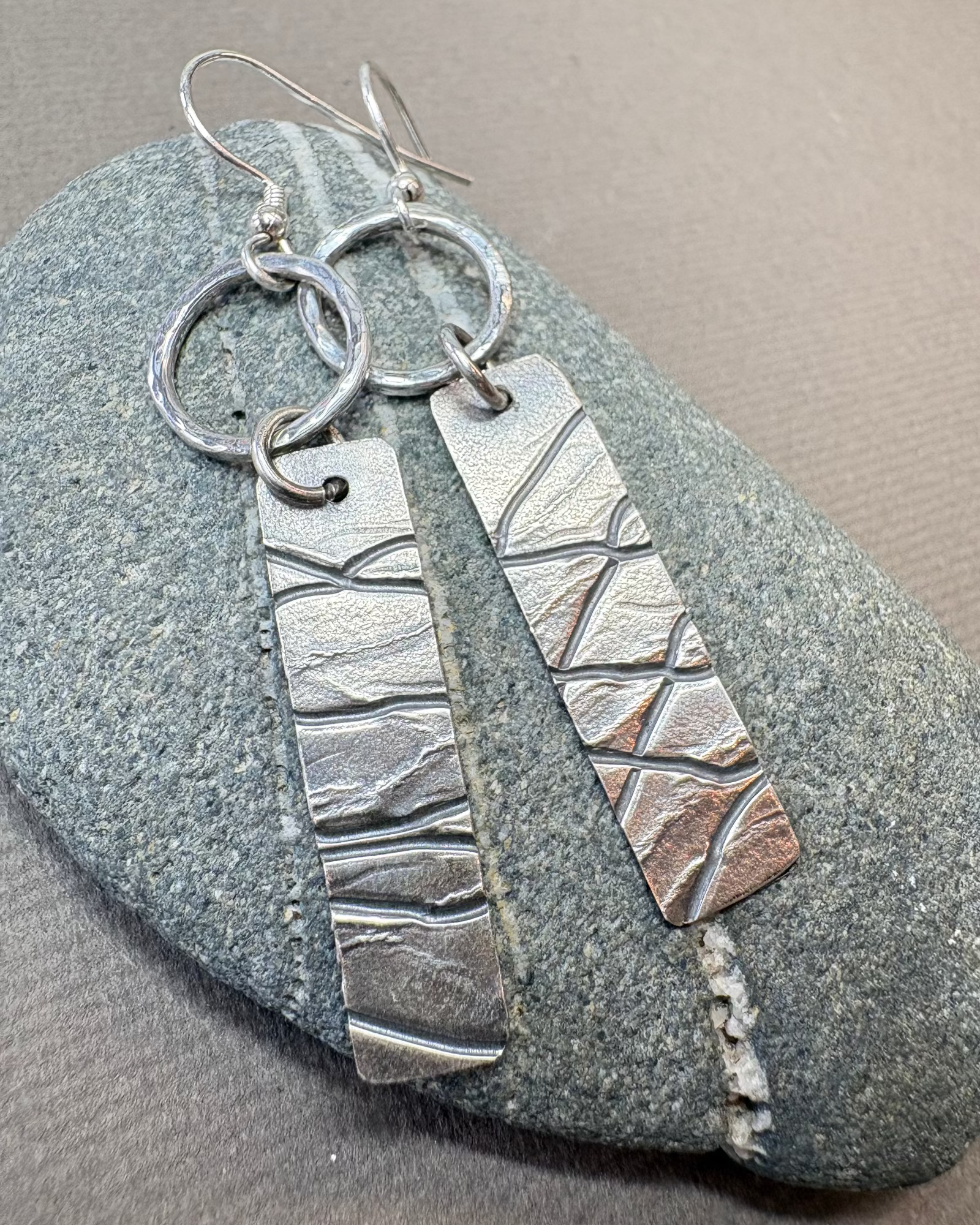 Silver hoop earrings with textured design on a pebble surface