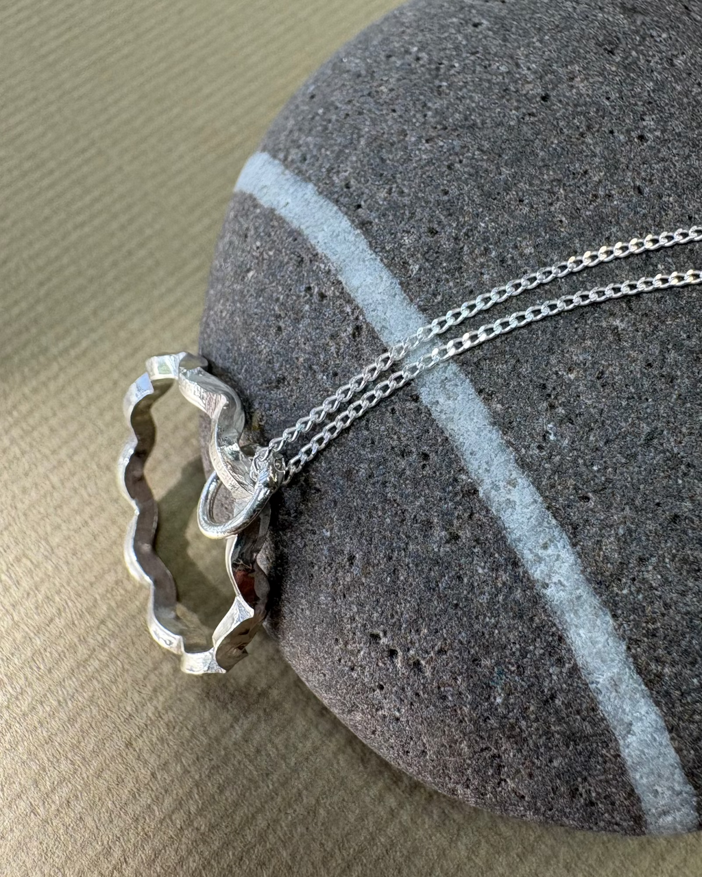 Silver necklace with a circular wavy pendant on a grey pebble surface