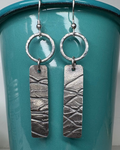 Silver earrings with textured rings and bars hanging from a teal cup