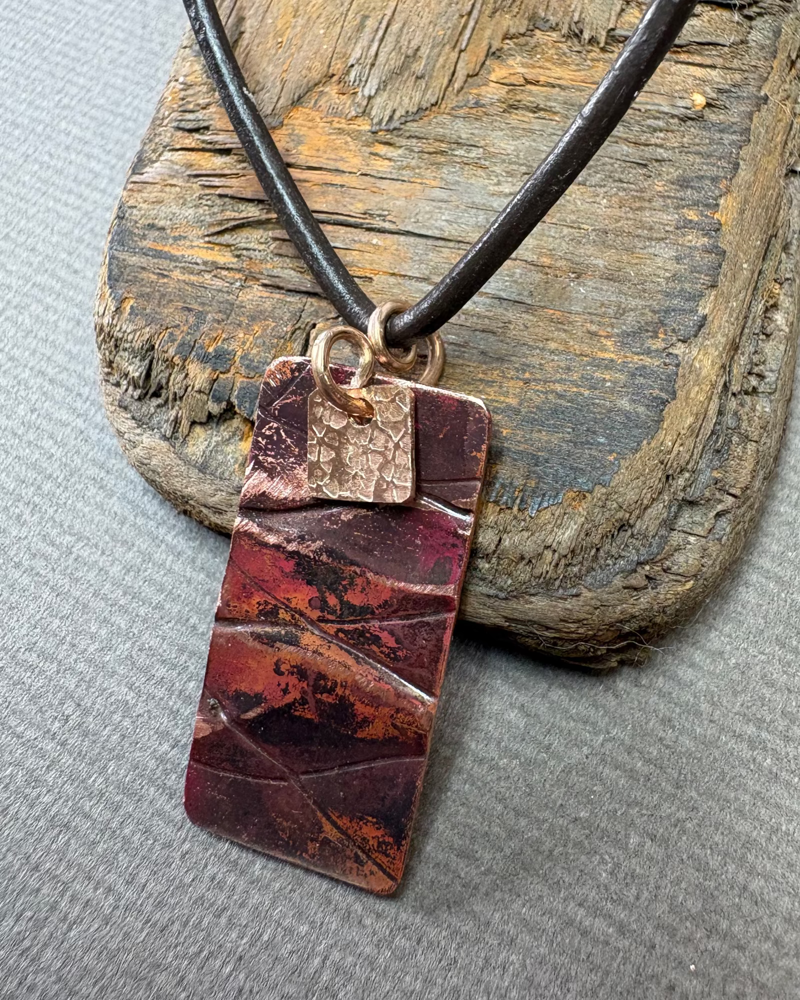 Necklace with a rectangular oxidised copper pendant on a driftwood block