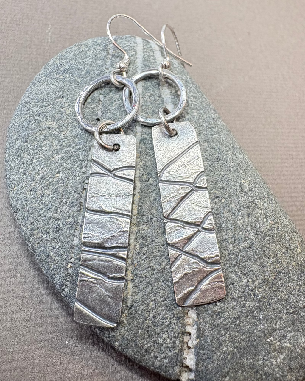 Silver hoop and textured earrings on pebble surface