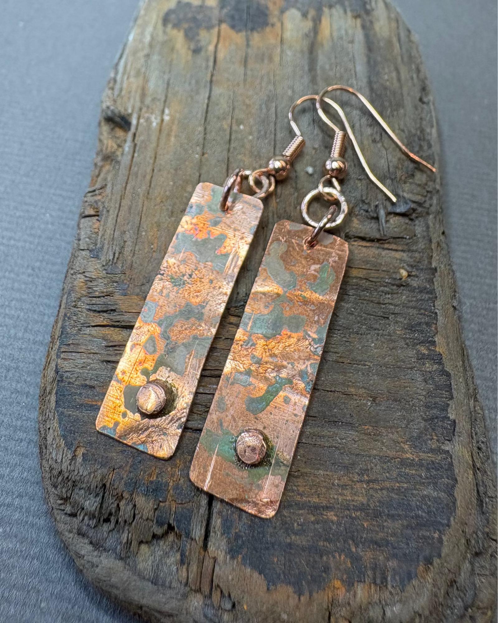 Pair of oxidised copper earrings with raised circle on a driftwood background