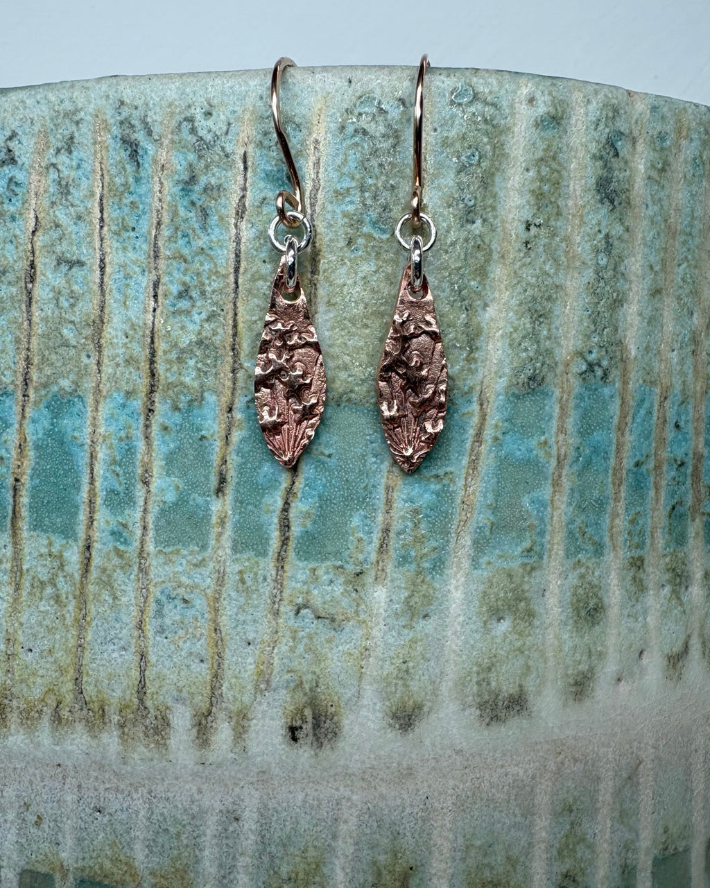 Pair of flower textured copper earrings on a ceramic vase
