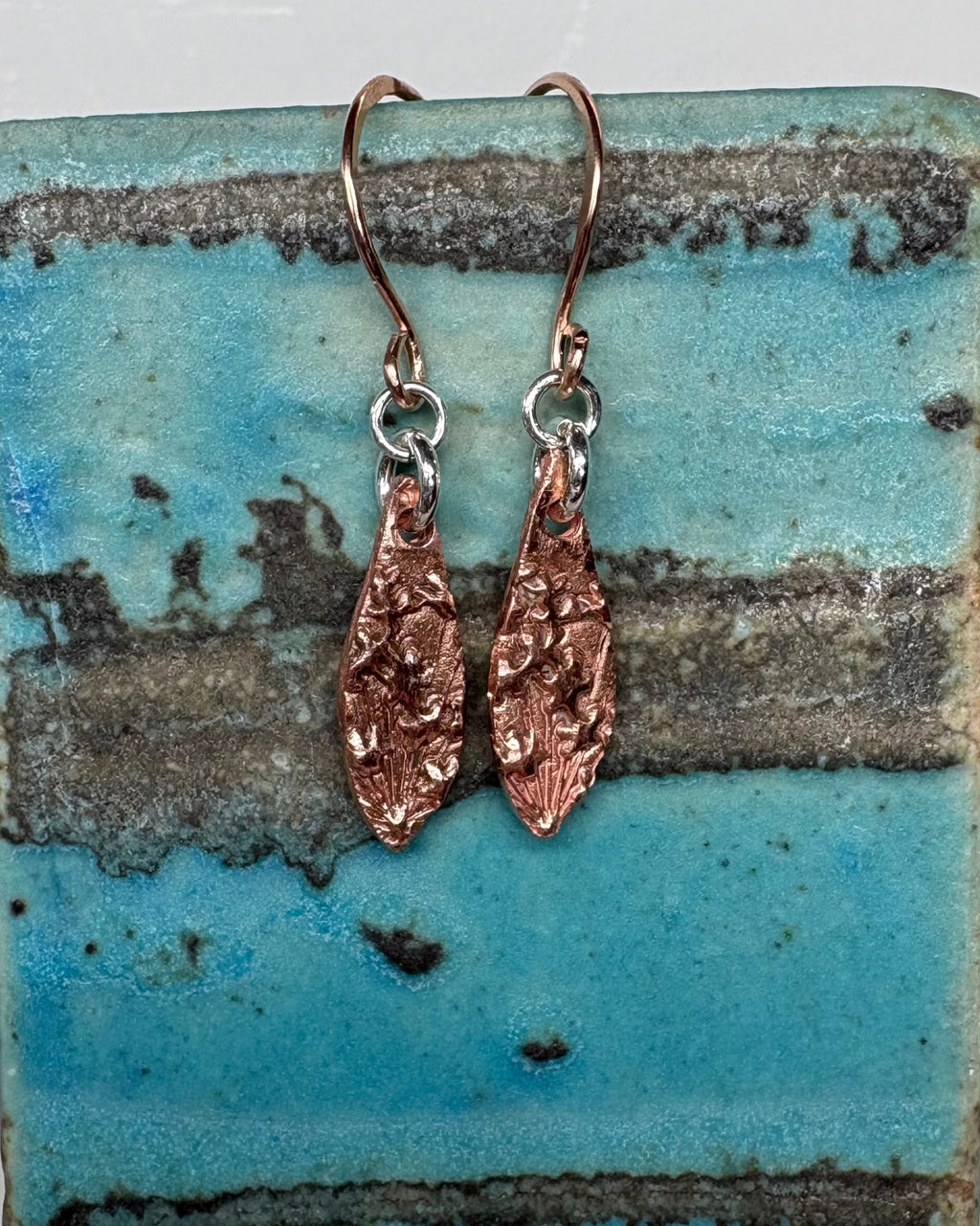 Pair of textured copper earrings on a ceramic vase
