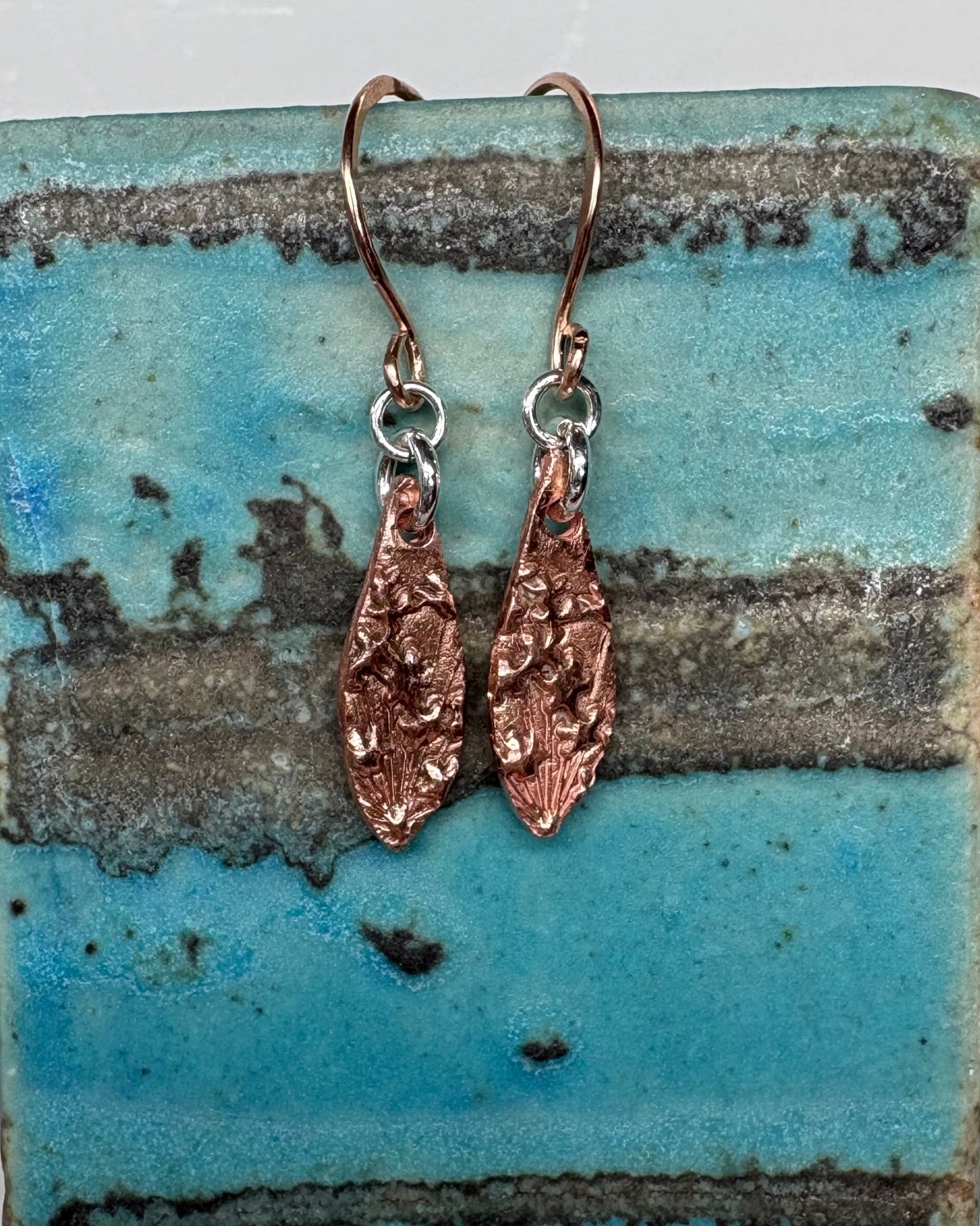 Pair of textured copper earrings on a ceramic vase
