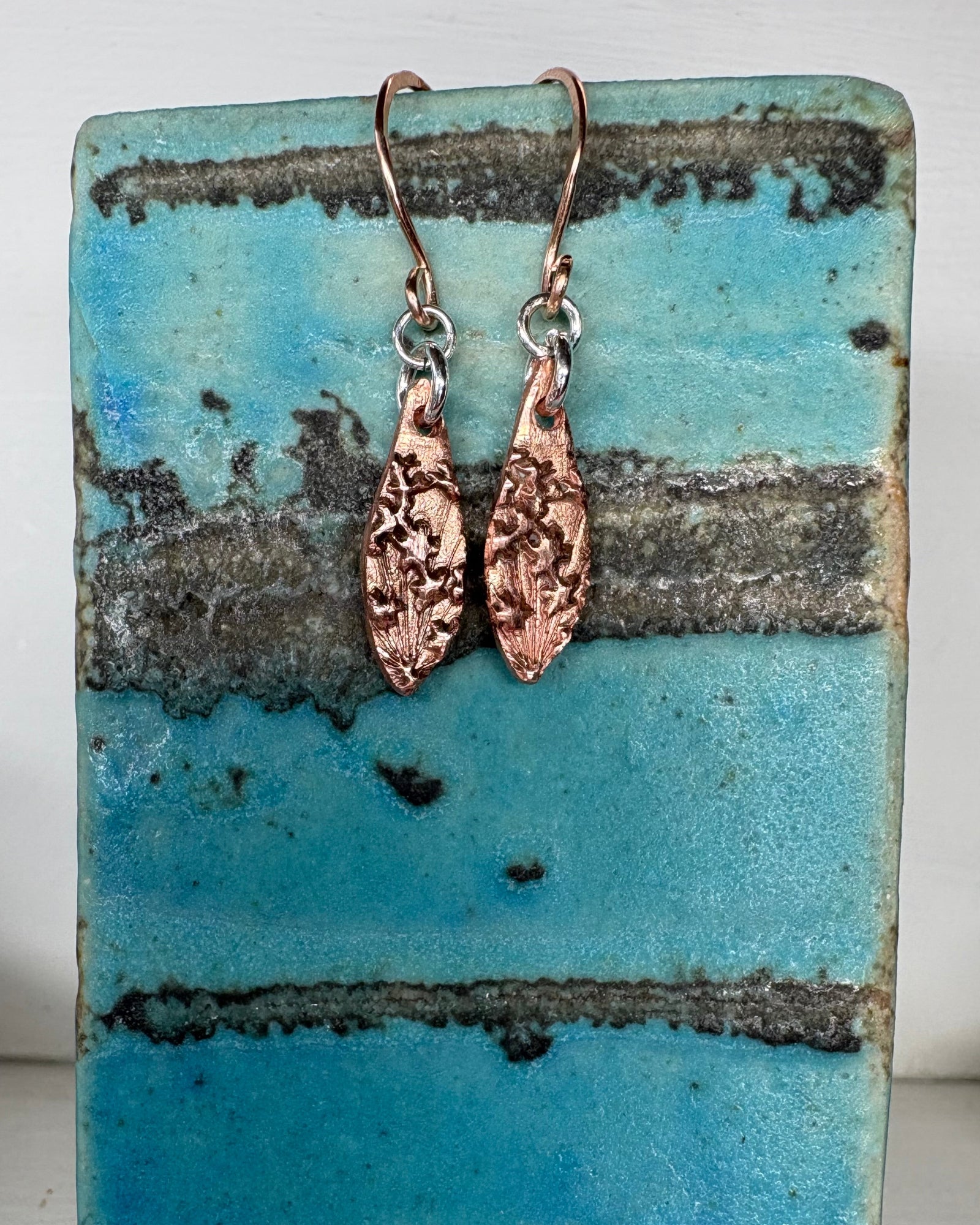 Pair of flower textured copper earrings on ceramic vase