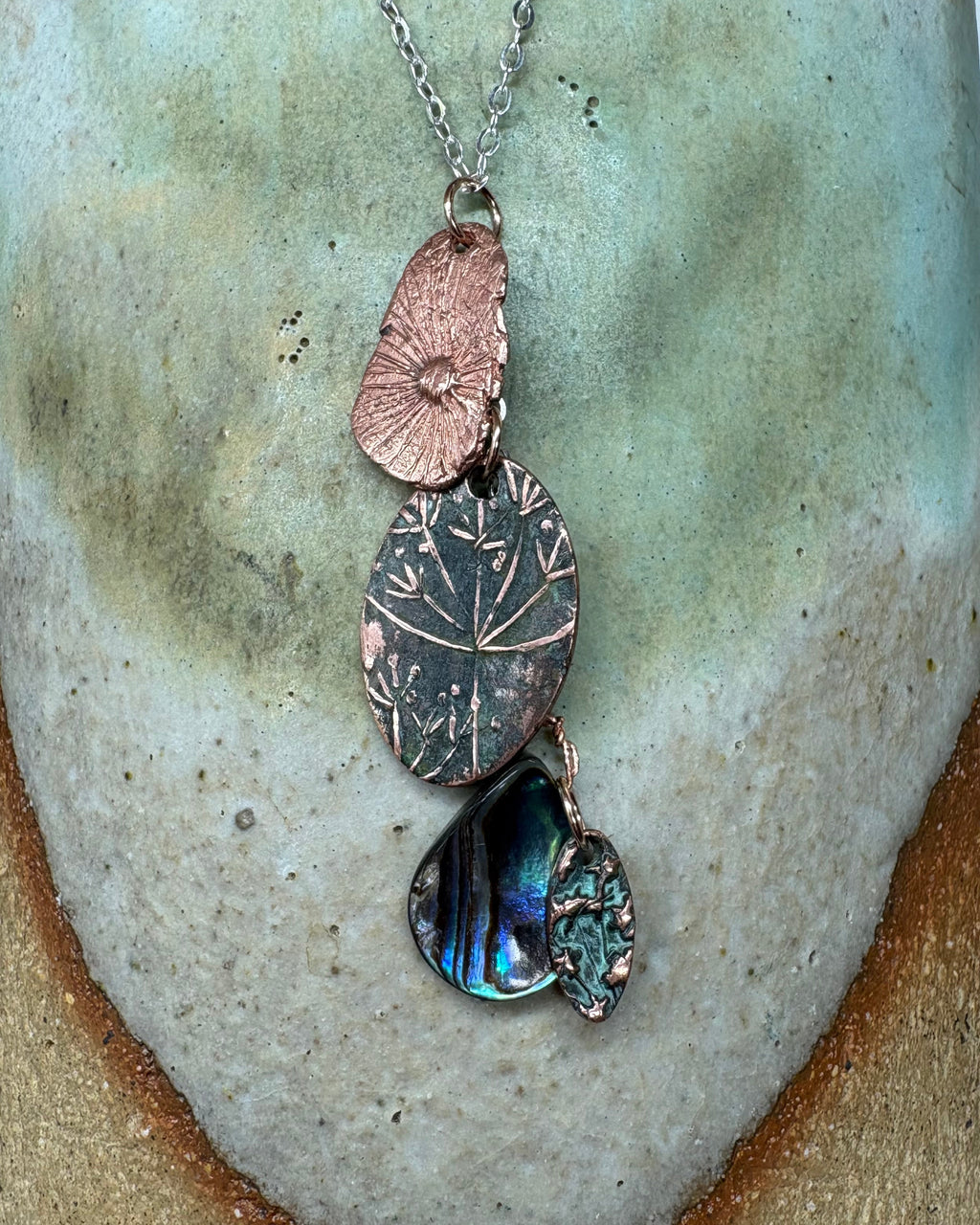 Necklace with flower head and paua shell charms on a silver chain on a ceramic surface