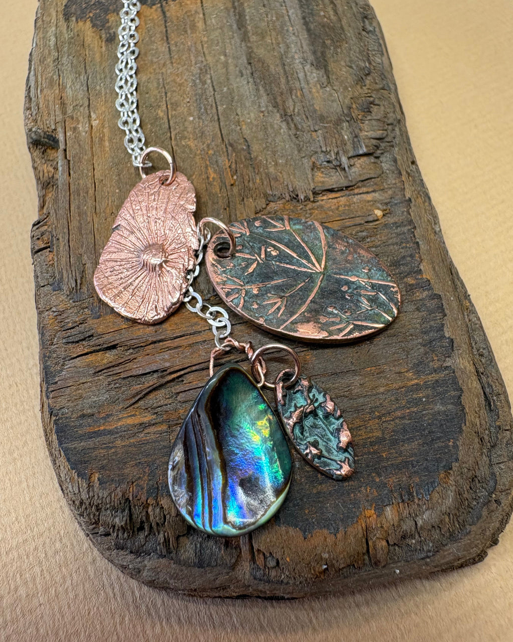 Necklace with flower head and paua shell charms on a silver chain on a wooden surface