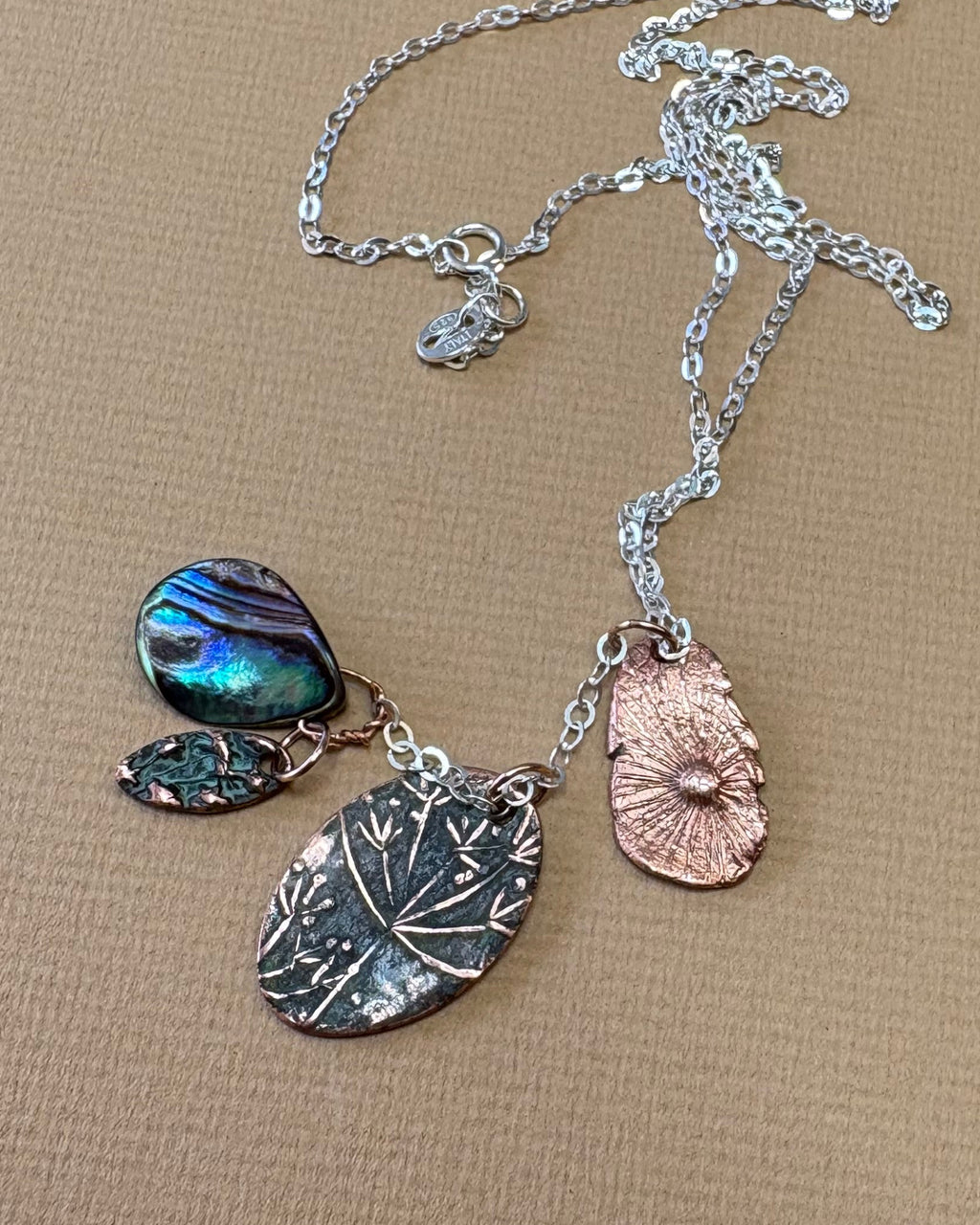 Necklace with flower and paua shell charms on a beige surface