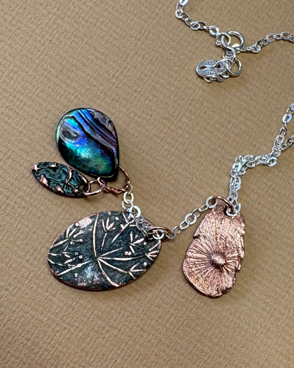 Necklace with flower and paua shell charms with a silver chain on a beige surface