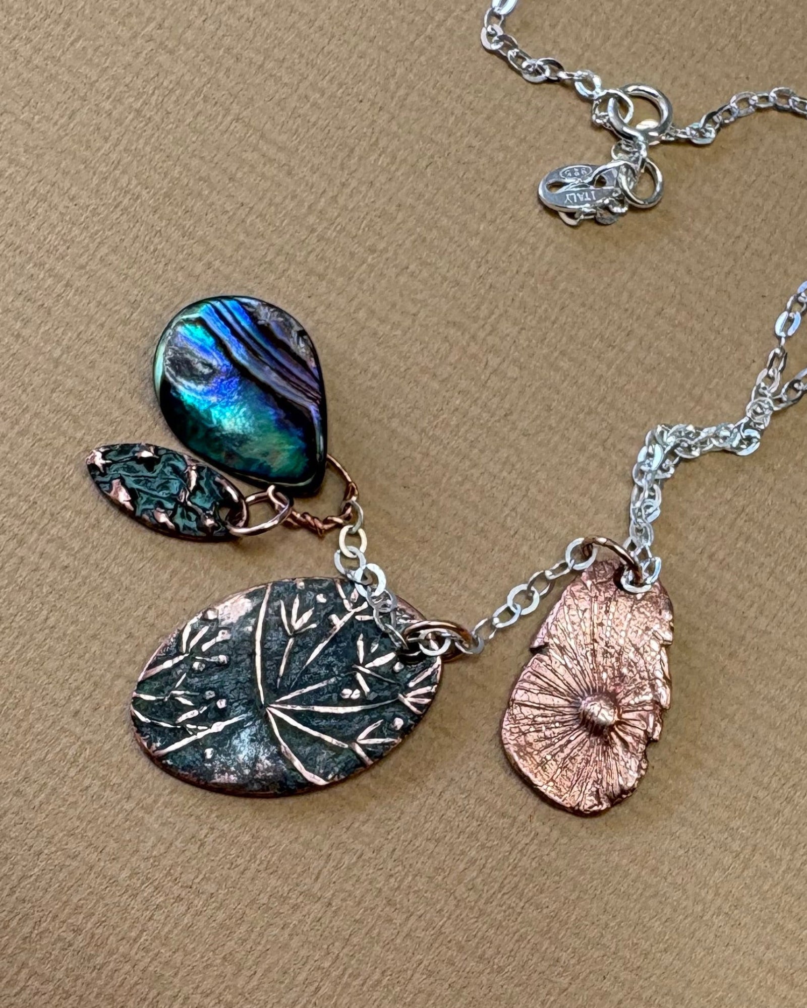 Necklace with flower and paua shell charms with a silver chain on a beige surface