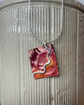 A handmade fire oxidised copper pendant necklace with pressed ripples and silver wavy design. This hangs from silver chain on ceramic vase.