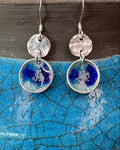 round silver concave enamel disc earrings with blue, aqua and silver to look like pools, with second hammered silver circle disk above, hung on silver ear wires. Pictured on a blue raku vase